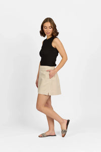 Woman in beige high-waisted shorts with side pocket, black sleeveless top, and slide sandals
