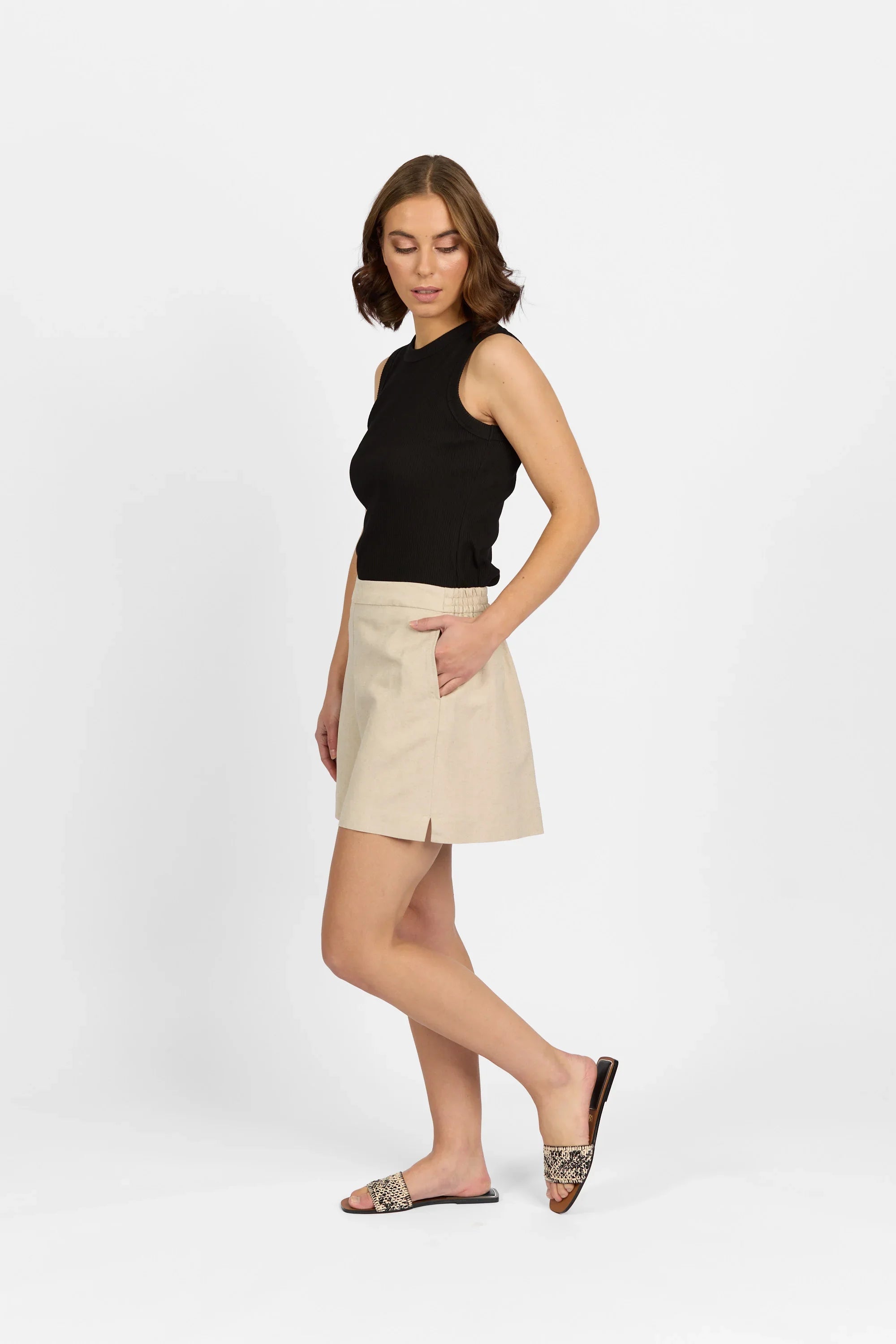 Woman in beige high-waisted shorts with side pocket, black sleeveless top, and slide sandals
