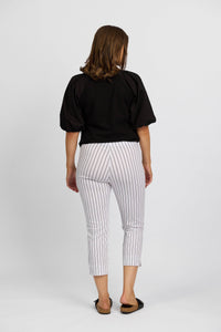 A woman faces away, wearing a black short-sleeve top and Vassalli Paris Printed Crop Pant in white with thin black stripes, made from stretch fabric, paired with black slip-on shoes, set against a plain white background.
