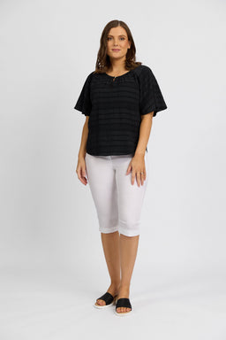 A woman with shoulder-length brown hair wears the Vassalli Paris Short in white and a black stretch top, styled with black slide sandals, against a plain white background. She faces the camera with a neutral expression.