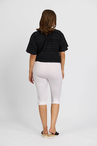 A person with shoulder-length brown hair, wearing a black short-sleeve top and Vassalli Paris Short - White, stands facing away from the camera against a plain white background.