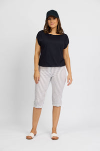 A woman stands facing the camera against a plain white background, wearing a black cap, black short-sleeved top, and Vassalli's Paris Printed Short in white with stripes.