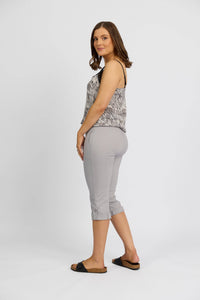 A woman with shoulder-length brown hair stands sideways in a sleeveless patterned top, Vassalli Paris 3/4 Cargo Short in Silver, and black slide sandals against a plain white background.