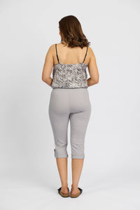 A woman faces away in a sleeveless patterned top with thin straps, Vassalli Paris 3/4 Cargo Shorts in Silver, and black flats, standing against a plain white background.
