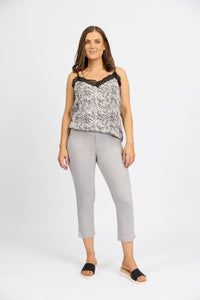 A woman with shoulder-length brown hair and a neutral expression wears a sleeveless patterned top with lace trim, Vassalli Paris Tour Capri pants in Silver, and black slide sandals against a plain white background.