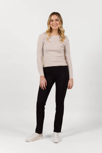 A woman with long blonde hair, in a light long-sleeve top, white shoes, and Vassalli Bay Pull On - Black Bliss pants, stands smiling against a plain white background.