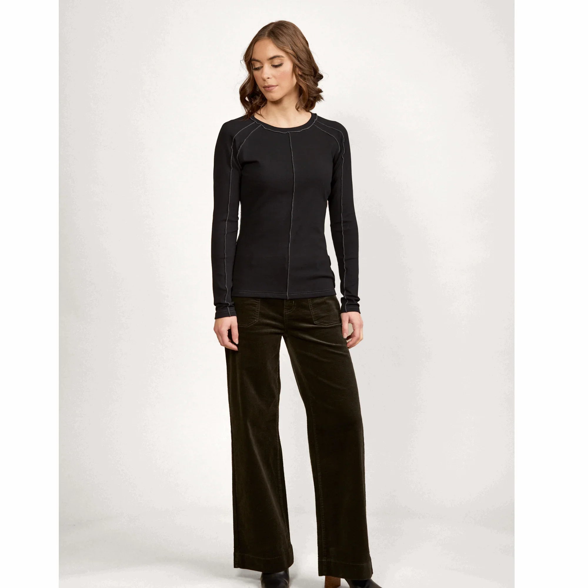 Woman wearing black long sleeve top and dark wide leg pants, studio background