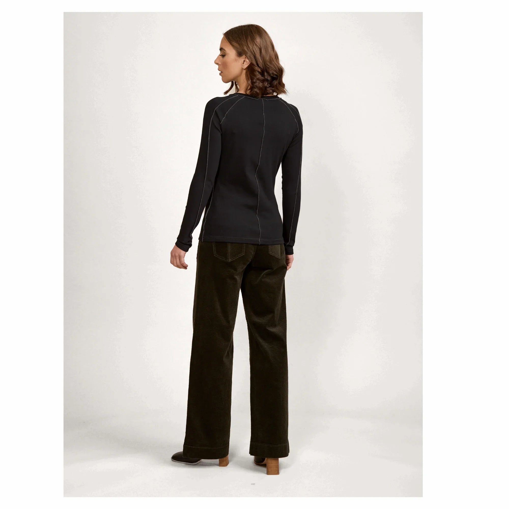 Woman in black long-sleeve top and wide-leg dark pants, shown from the back, studio setting