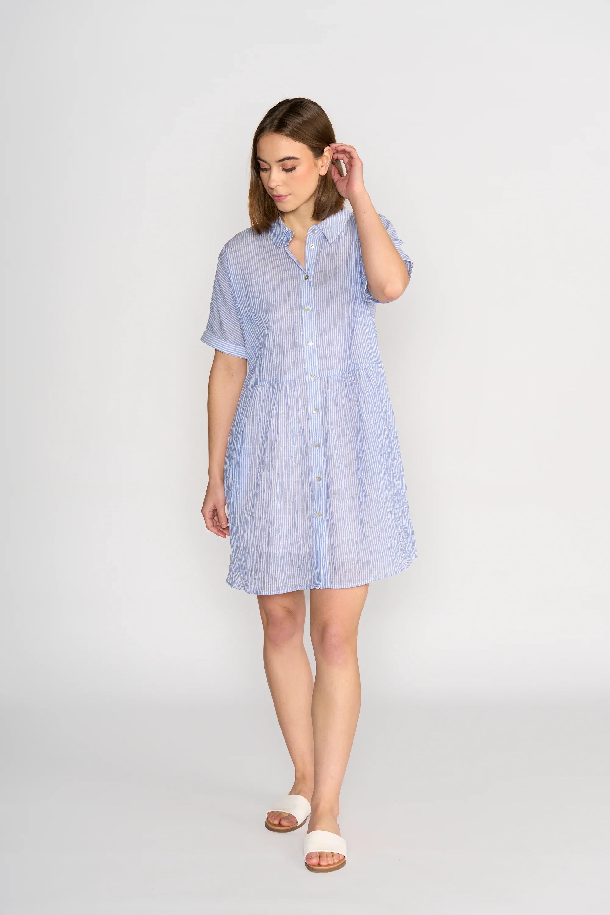 Woman wearing a short-sleeve blue striped button-up cocoon dress, standing indoors.