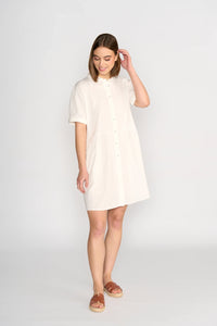 Woman wearing short-sleeve off-white cocoon dress with button front and sandals