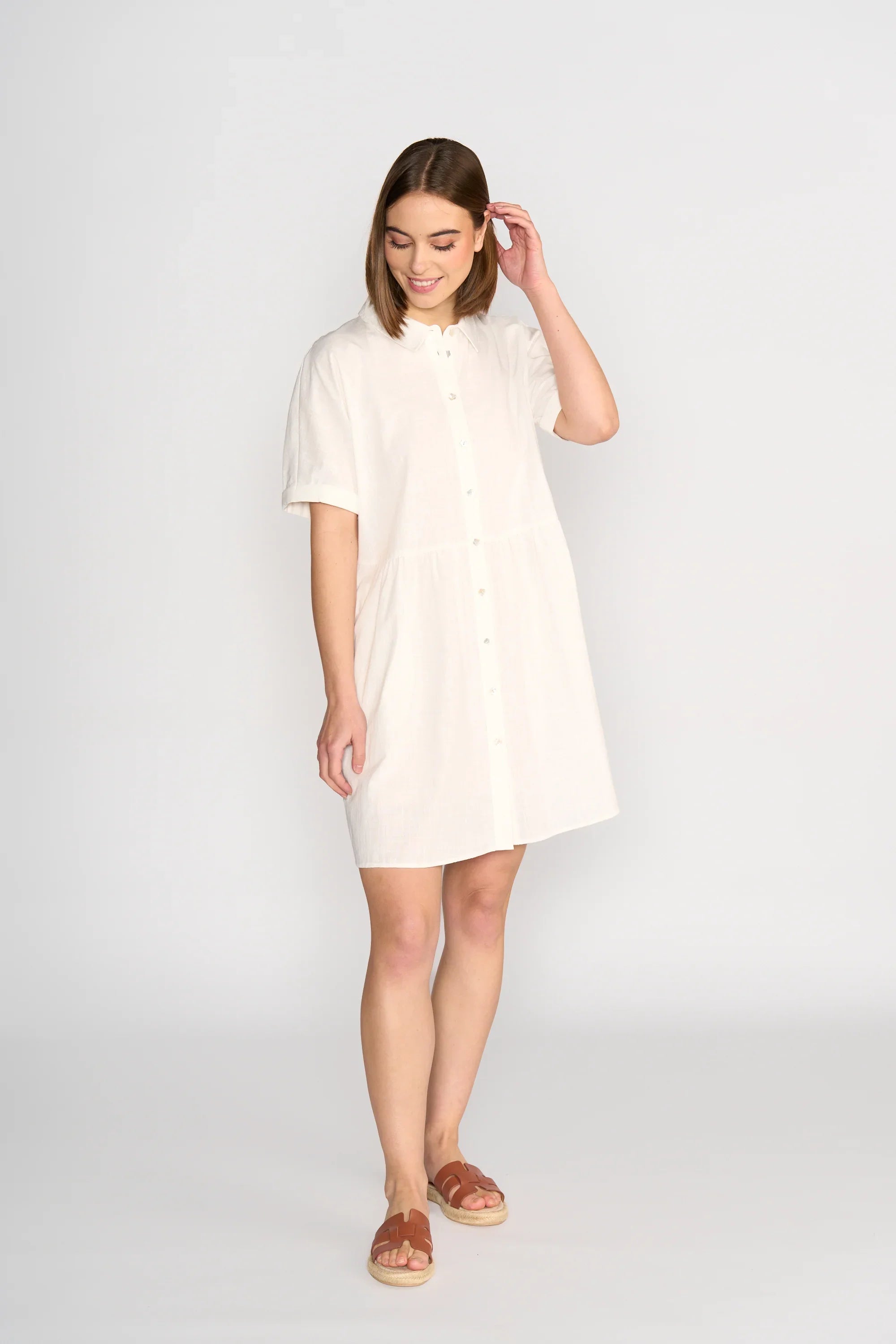 Woman wearing short-sleeve off-white cocoon dress with button front and sandals