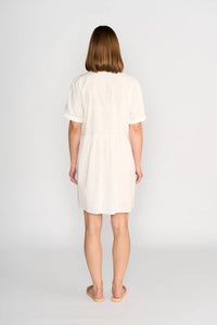 Woman wearing off-white short sleeve cocoon dress, standing barefoot, back view