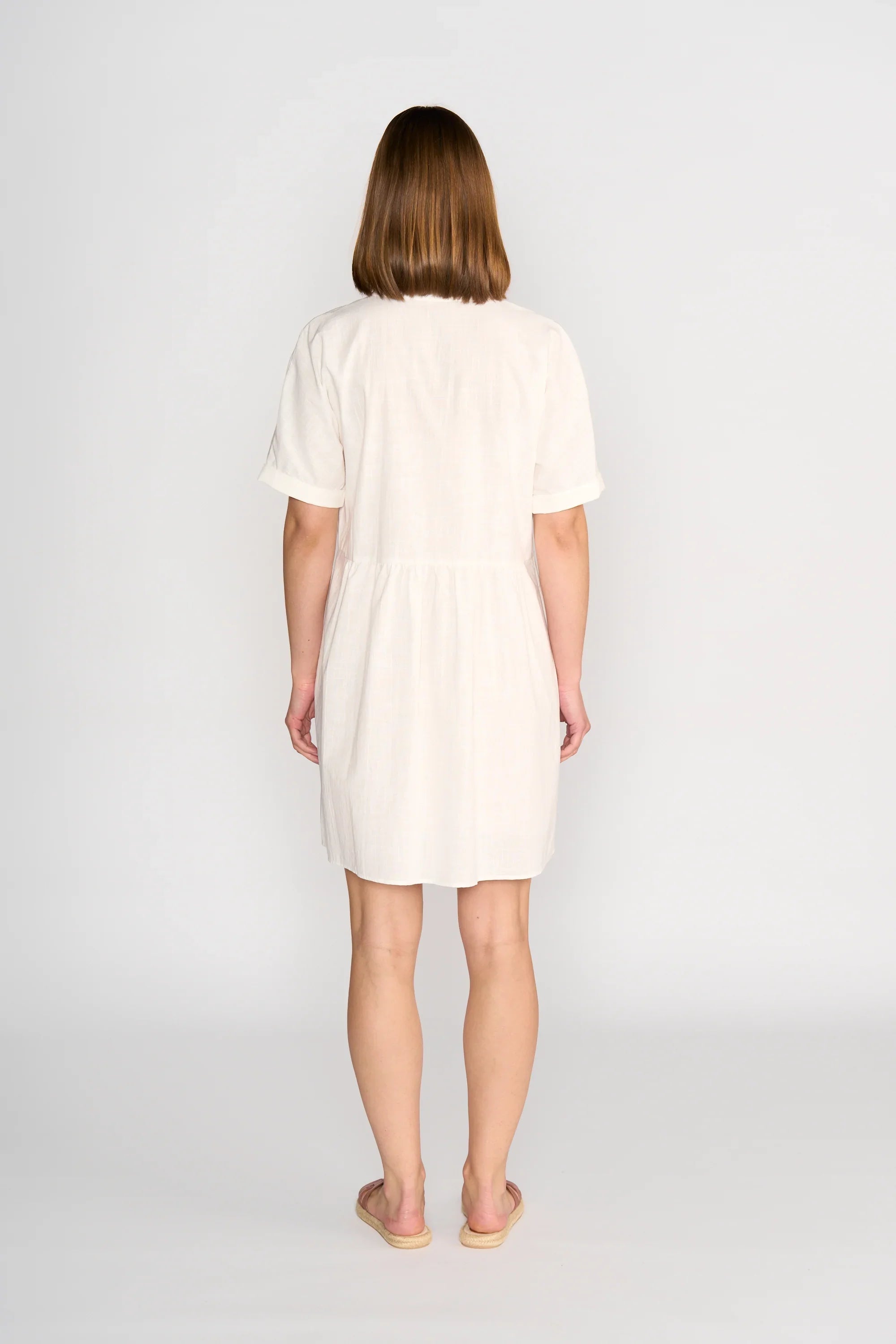 Woman wearing off-white short sleeve cocoon dress, standing barefoot, back view