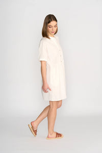 Woman wearing off-white cocoon dress with short sleeves and brown sandals, side view