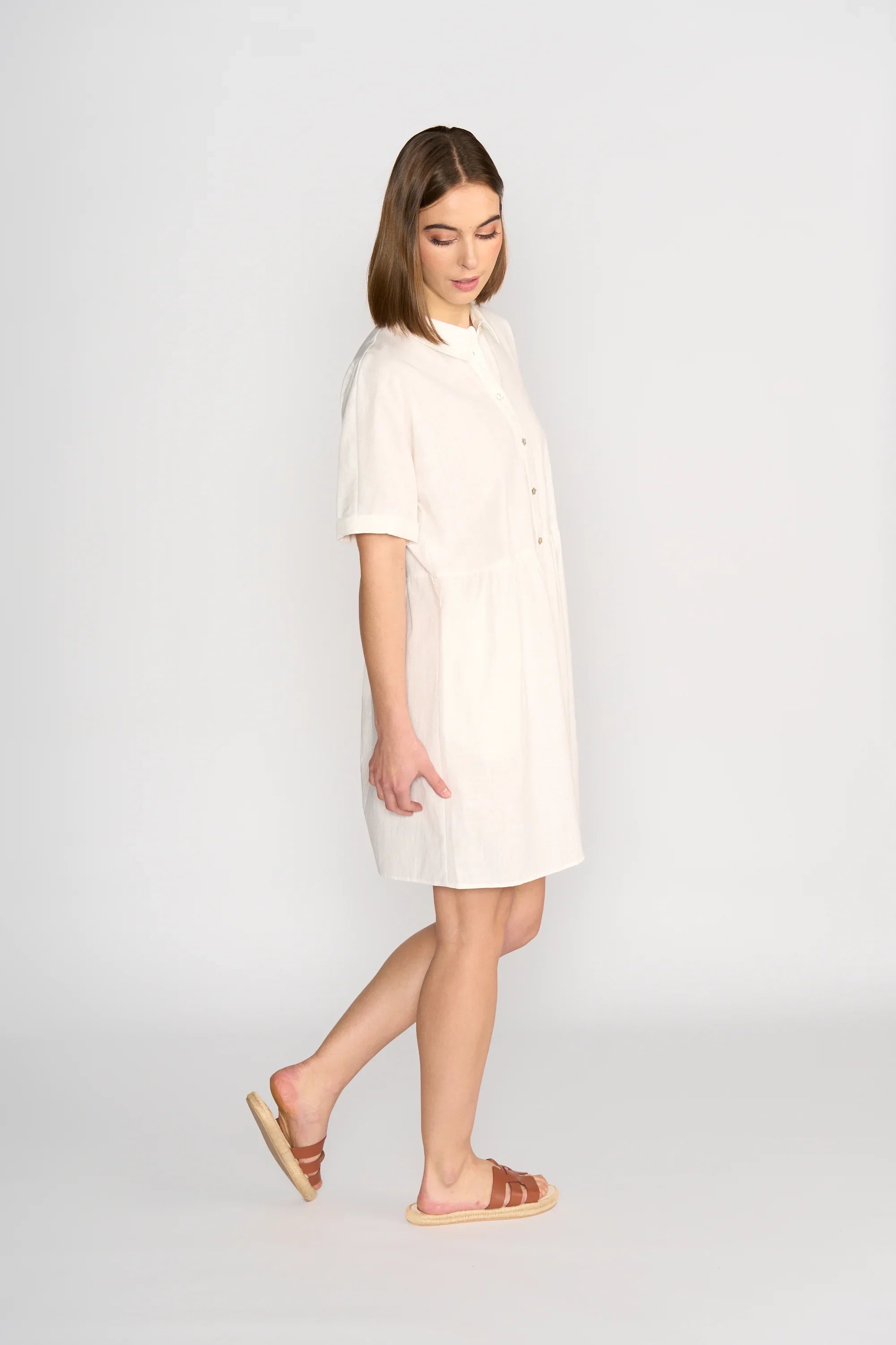 Woman wearing off-white cocoon dress with short sleeves and brown sandals, side view