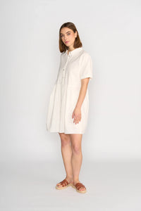 Woman wearing off-white cocoon dress with short sleeves and button front, standing against plain background