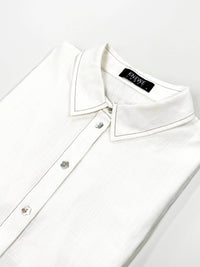 Folded off-white cocoon dress shirt with floral buttons and pointed collar on white background