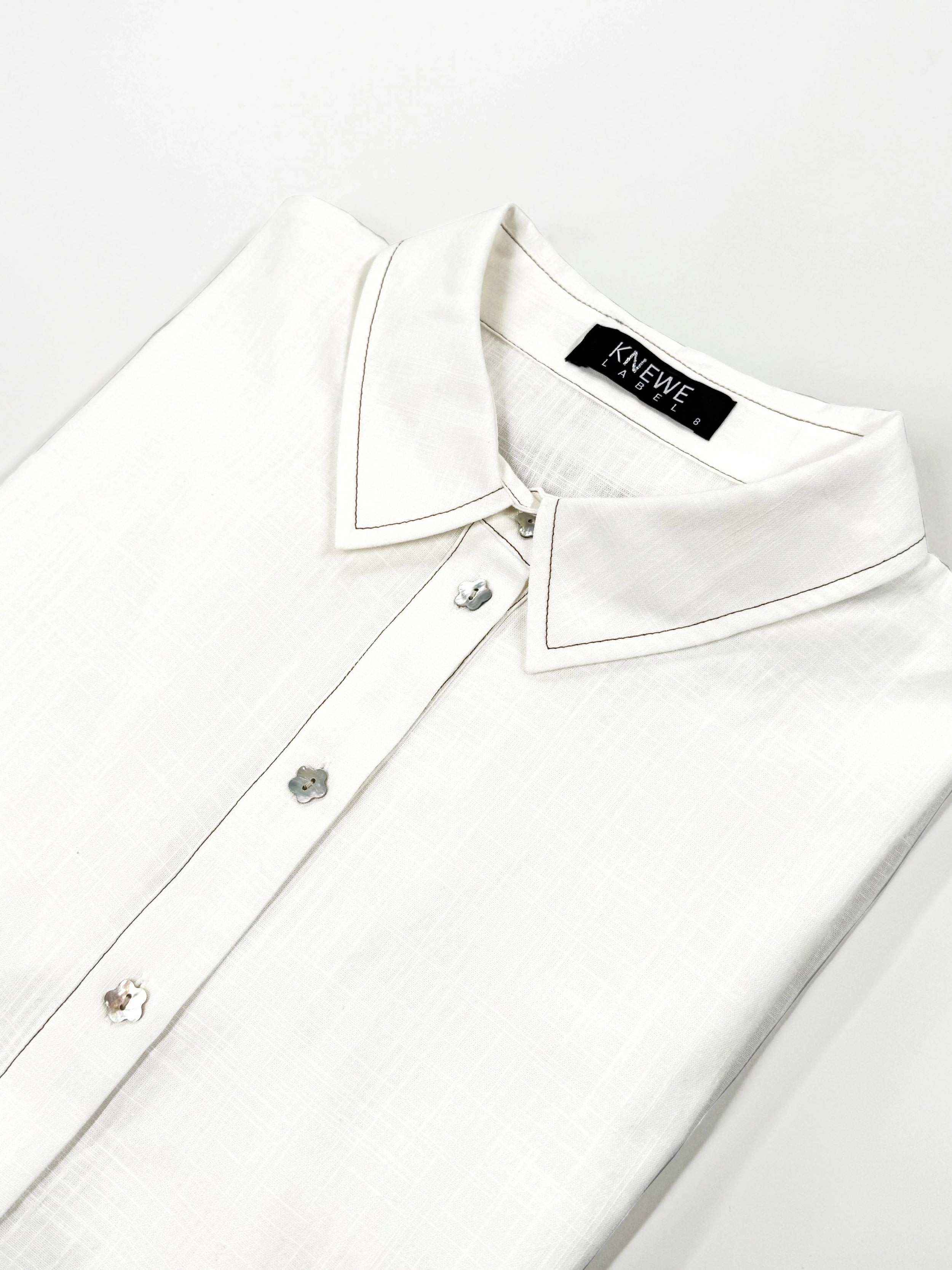 Folded off-white cocoon dress shirt with floral buttons and pointed collar on white background
