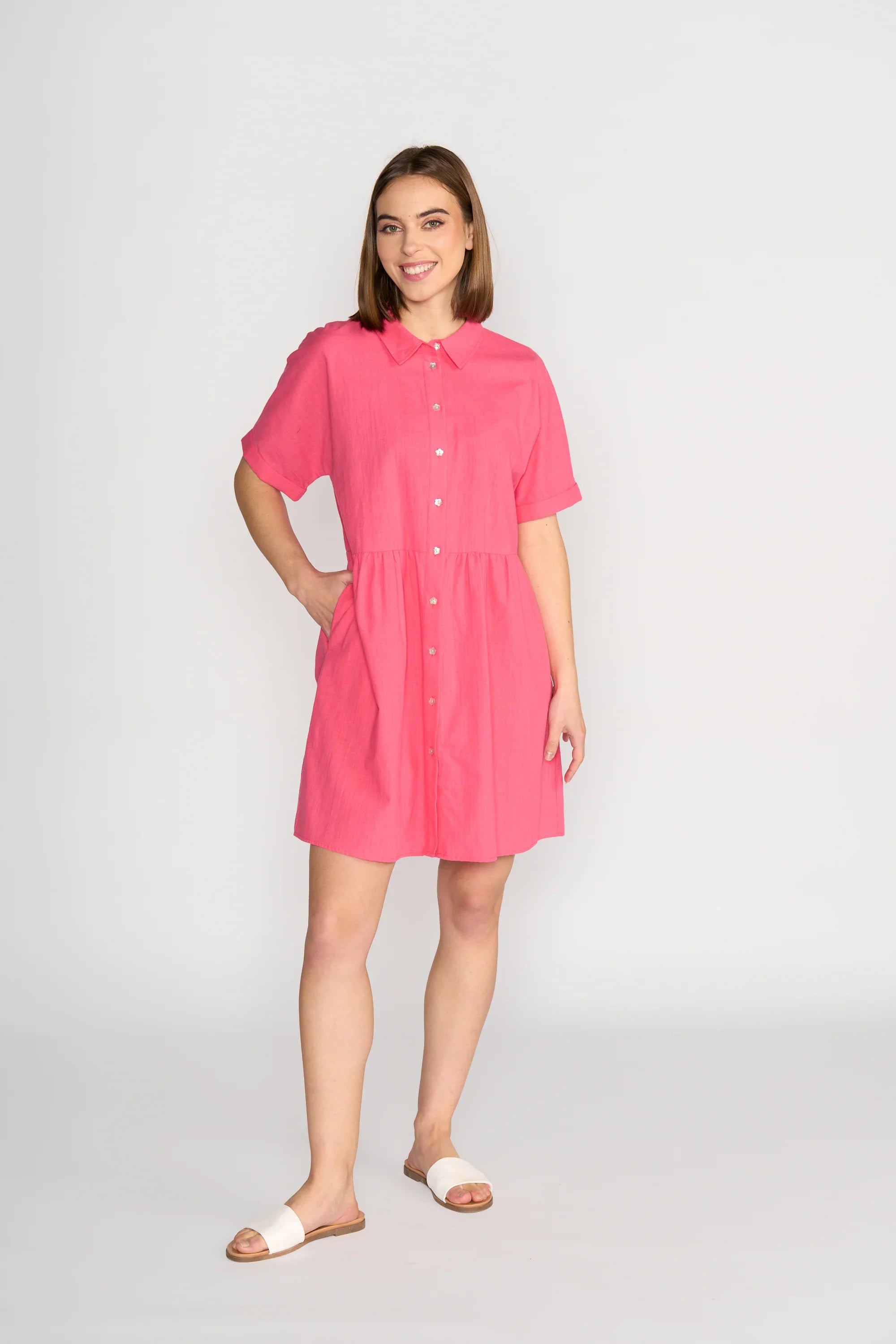 Woman wearing short-sleeve raspberry pink cocoon dress with buttons, standing in studio