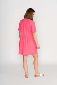 Woman wearing short sleeve raspberry cocoon dress, viewed from the back, with white sandals.
