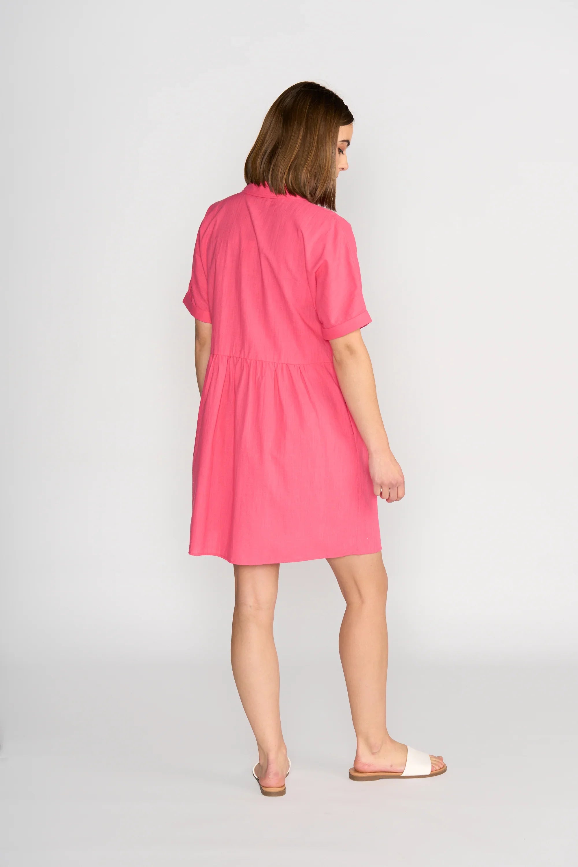 Woman wearing short sleeve raspberry cocoon dress, viewed from the back, with white sandals.