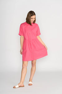 Woman wearing short sleeve raspberry pink button-front cocoon dress, white sandals