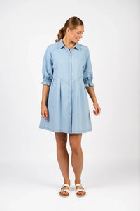 Woman wearing light wash denim shirt dress with three-quarter sleeves and white sandals