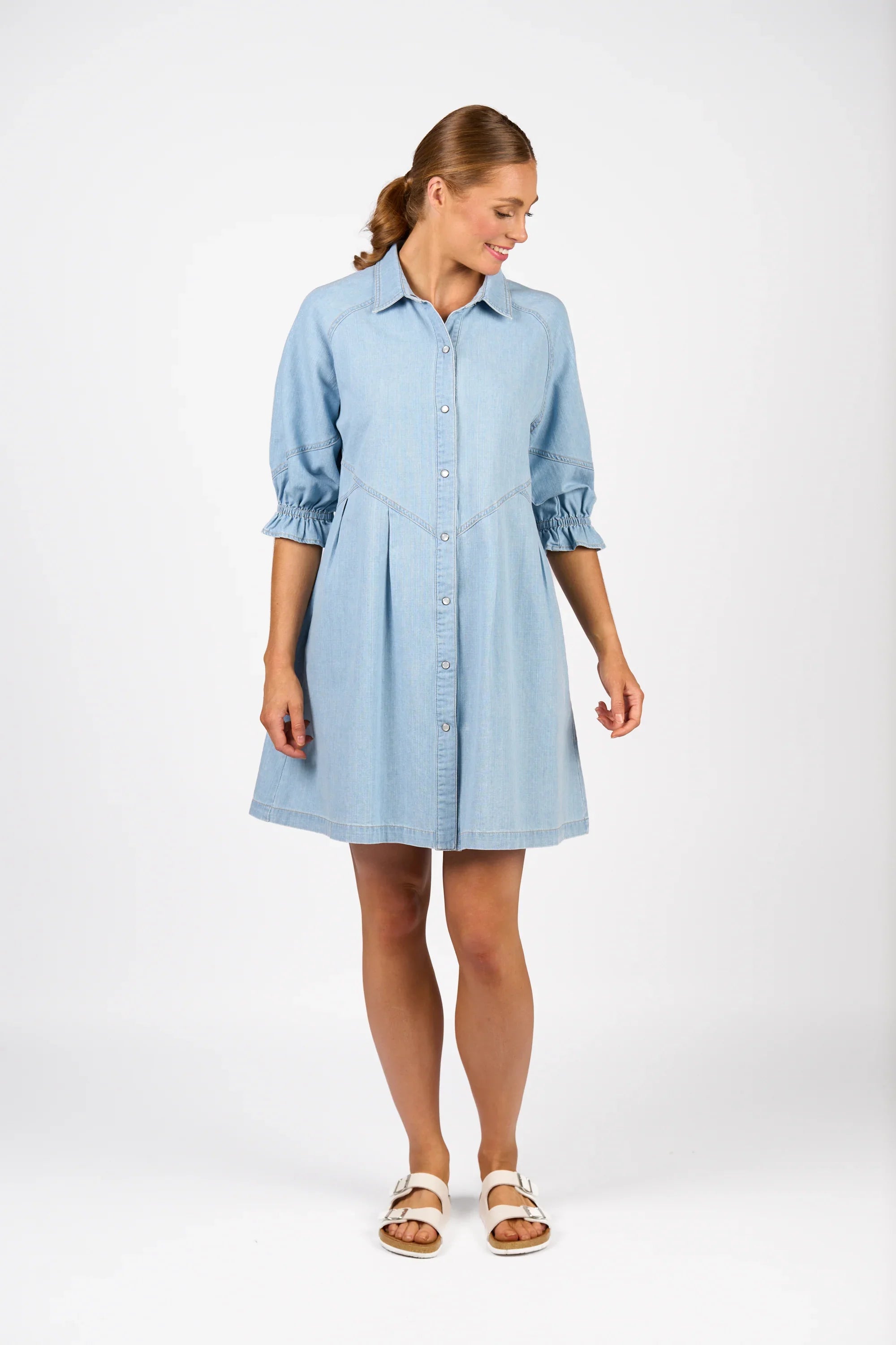 Woman wearing light wash denim shirt dress with three-quarter sleeves and white sandals