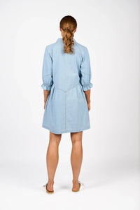 Back view of woman wearing light blue denim dress with puff sleeves, white flat shoes