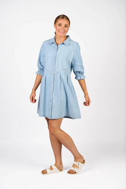 Woman wearing a light wash denim shirt dress with 3/4 sleeves and button front, against white background