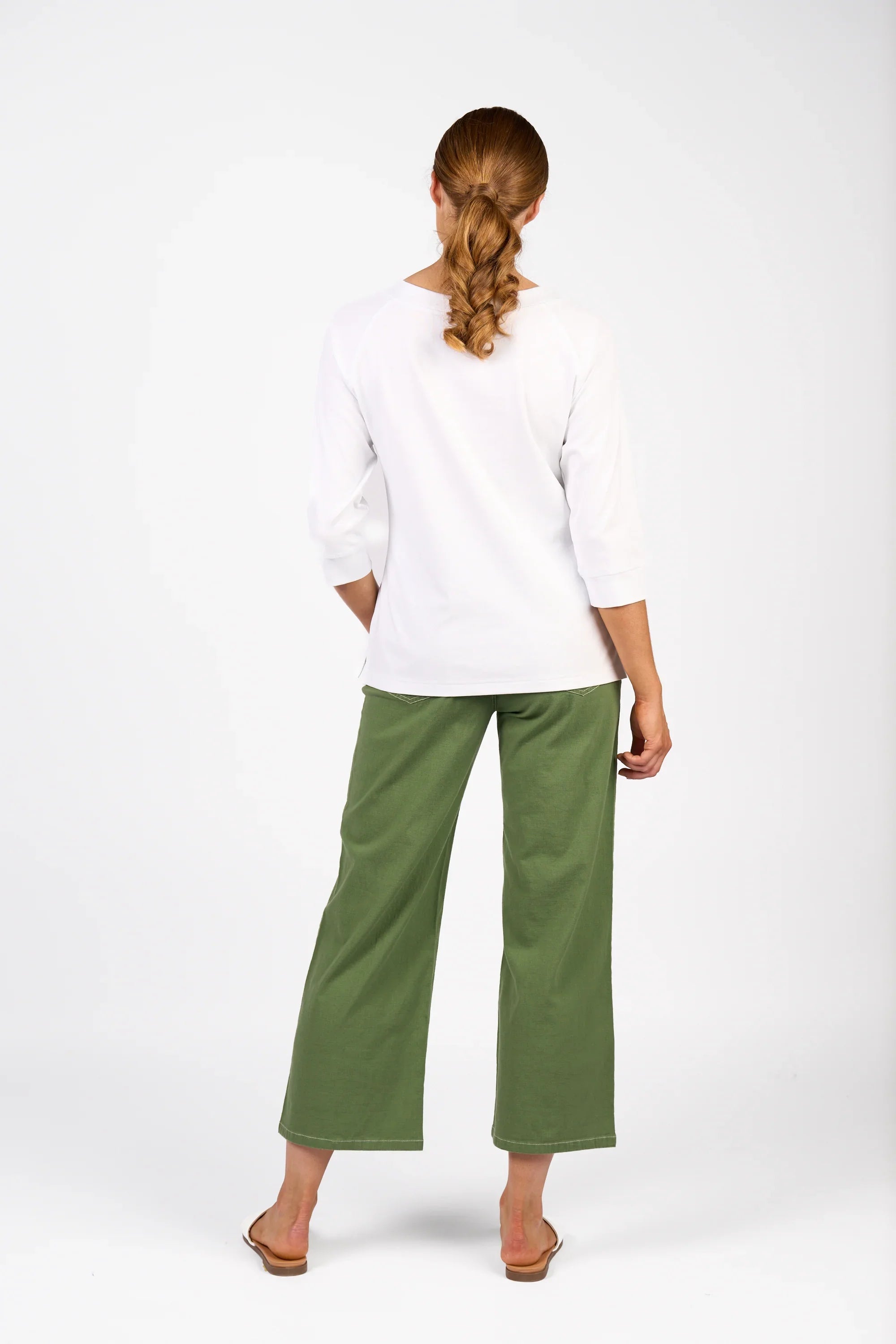 Woman wearing a white three-quarter sleeve tee and green wide-leg pants, rear view