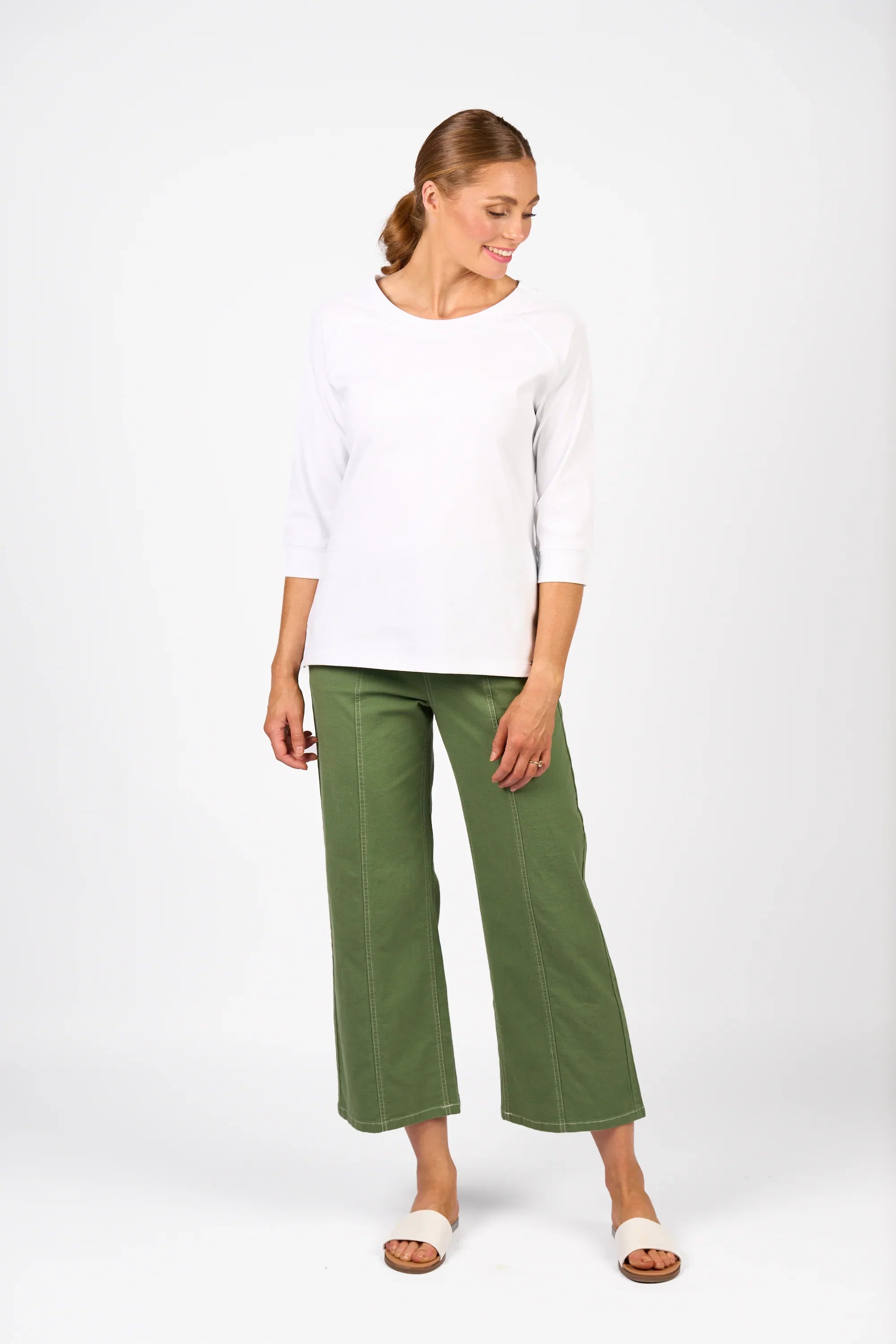 Woman in a white three-quarter sleeve tee and green wide-leg pants, standing, studio background