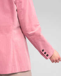 A person wears the Vassalli Gallery Blazer in dusky pink, featuring black sleeve buttons and a soft pinwale cord texture, shown from the back and side with a slightly bent arm, set against a plain light gray background.