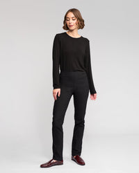 A woman with short brown hair stands against a plain background, wearing Vassalli's Bay Pull On - Black pants and a long-sleeve black top, paired with dark red loafers. She looks slightly to the side with a relaxed expression.