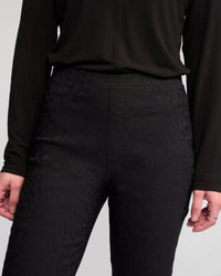 A person models the Vassalli Bay Pull On - Black, a long-sleeved top and high-waisted slim pants with subtle animal texture, shown from shoulders to mid-thigh. Hands rest at their sides; one hand wears rings.