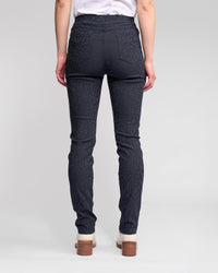 A person is seen from behind wearing Vassalli Bay Pull On - Navy pants, featuring an animal texture, back pockets, and an elastic waistband. They pair the slim-fit pants with a white shirt and light-colored heeled shoes.