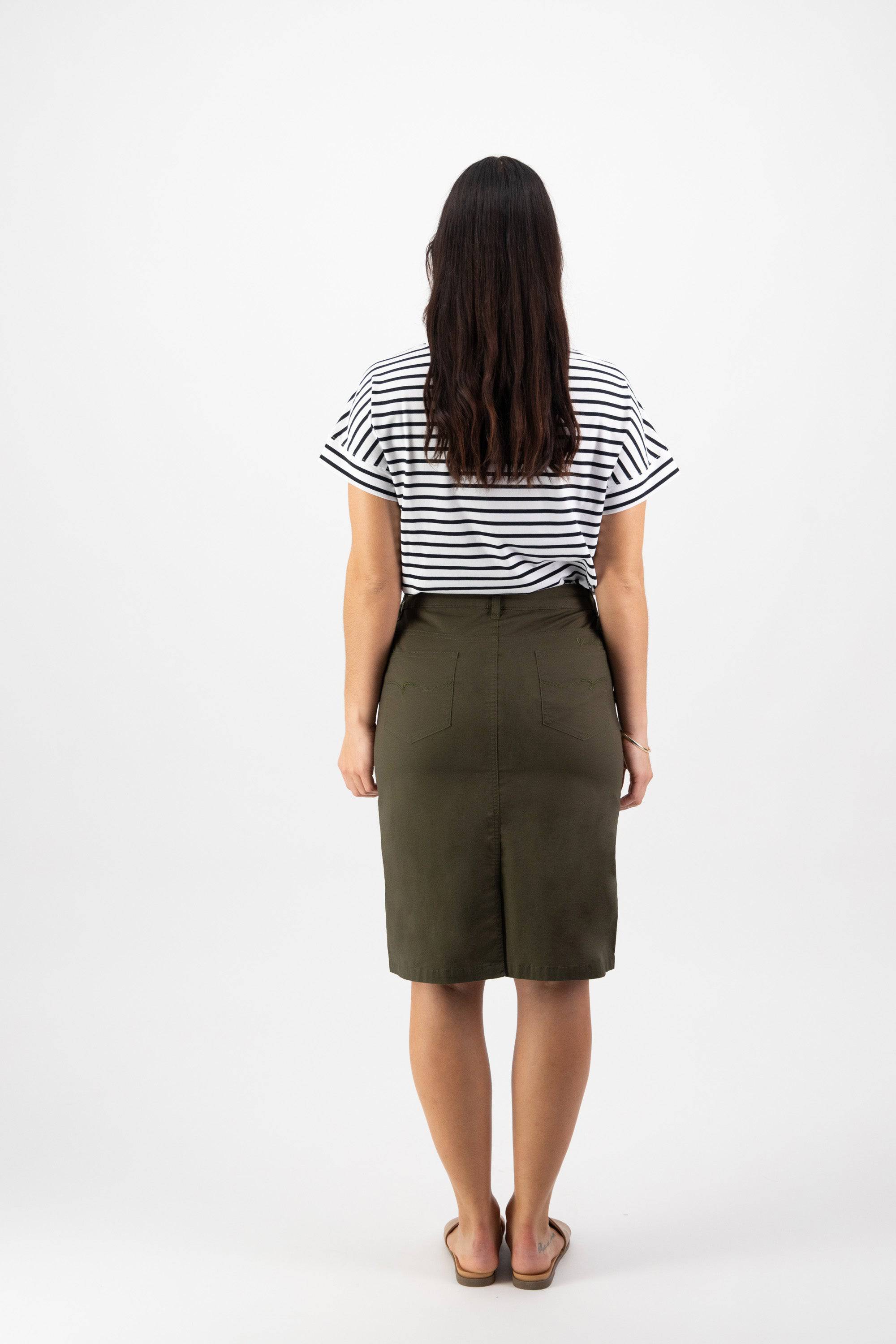 A woman, seen from behind, wears a black and white striped shirt, brown sandals, and the Vassalli Poppy Poplin Skirt in khaki, standing against a plain white background.