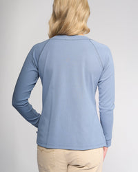 A person with blonde hair is facing away, wearing the Vassalli Key Top in denim blue and light beige pants, against a plain light background.