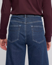 A person is shown from the back wearing a long-sleeve burgundy top and Vassalli Alley Jean - Dark Blue, featuring a high-waisted, wide-leg silhouette, ankle length, and two back pockets with decorative stitching.