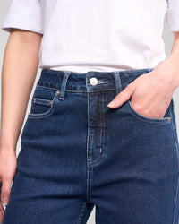 A person wearing a white t-shirt and Vassalli’s Wren Jean - Dark Blue, high-waisted with wide legs, with one hand in a front pocket. The photo is cropped to show the torso and upper legs.