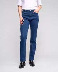 A person wears a white short-sleeve top, Vassalli Radio Jean - Blue Denim, and black ankle boots while standing against a plain light background.