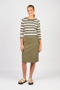A woman smiles against a light grey background, wearing a cream and black striped 3/4 sleeve top, the Vassalli Belen Skirt - Army, and beige buckle sandals.