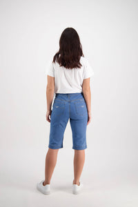 Back view of a woman wearing Vassalli Custom Short - Light Denim, featuring stretch fabric and back pockets, styled with a white short-sleeve T-shirt and white sneakers against a light grey background.